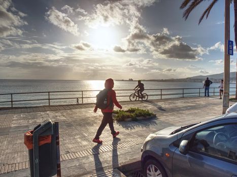 Woman hiker with backpack walk quickly  at sea via pomenade  at Palma de Mallorca city, 26th of January 2020