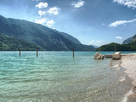Stony bathing beach lake with stack of sharp boulders. Beautiful clear and cold mountain lake in Alps.