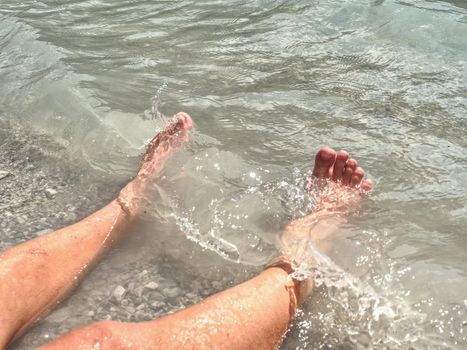 Naked legs along wave of lake water and rough white stony sand on the beach. Carefree and relaxing attitude