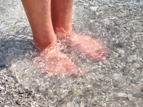 Hairy strong male legs are cooling in cold water of mountain lake. Green blue cold water of kaje in Dolomiti.