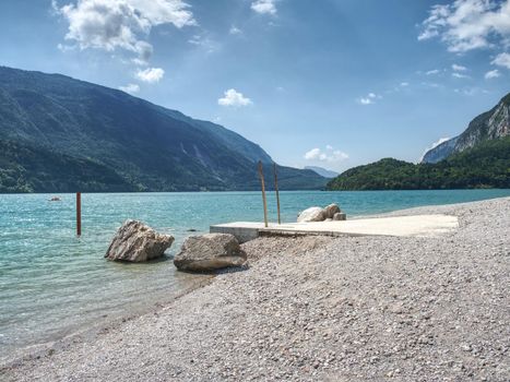 Stones stack on shore of blue green water of mountain lake. Blue mountains in water level mirror.