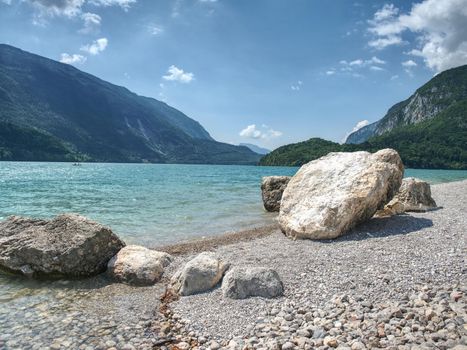 Stony bathing beach lake with stack of sharp boulders. Beautiful clear and cold mountain lake in Alps.