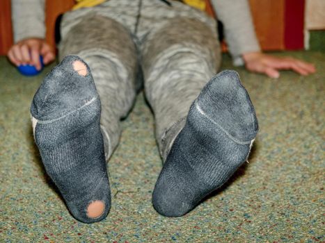Kid wearing dirty sweaty socks with holes in heel. Pink skin in soks hole