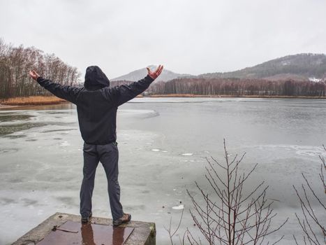 frozen wet  man stands on weir cover at pond with raised his hands