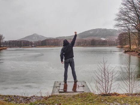 Cold rainy day at pond.  Wet man standing by the riverside 