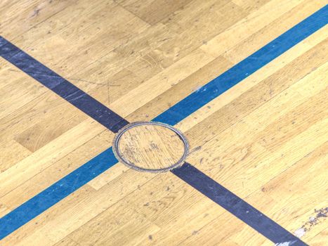 Circle cover plug for sport equipment in floor of school gym. Painted lines on wooden floor of sporting hall with sratched surface.