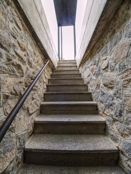 Interior of a narrow and steep staircase leading to the underground of the medieval castle. Glass box entrance