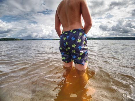 Teenager in water. Blond hair boy go swimming in the pond. Sunny spring day.