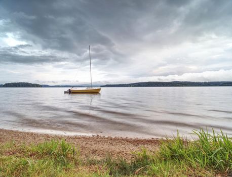 Sailing boat on calm waters. Empty yacht anchored at lake shore
