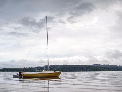 Small sailing boat anchoring next to a buoy in the calm water of lake, moody tones