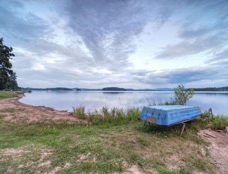 Simple rowing boat stacked at lake upside down. Empty beach at popular tourist resort. 