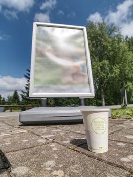 Holiday coffee cup. Aromatic coffee in takeaway paper cup on pavement in front of advertisment board. 14th of July 2019, Lipno, Czech Republic. 