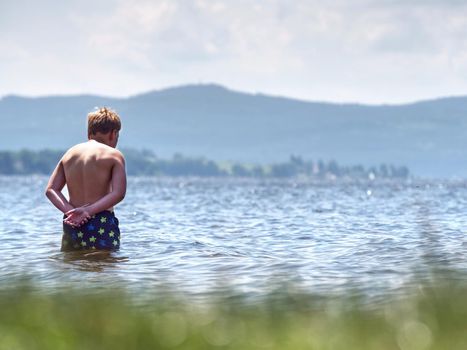 Teenager in water. Blond hair boy go swimming in the pond. Sunny spring day.