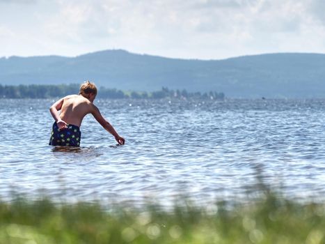 Boy stay in cold lake with water under knee and test temperature. Cold spring day for swim.