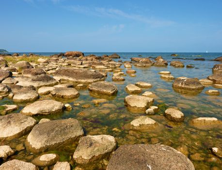 Big boulders in shore in  smooth wavy sea. Stony coastline, clear sky.