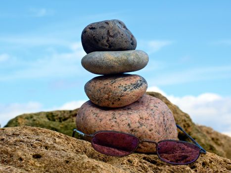 Pink summer glasses and stone pyramid on sea shore, waves in background. 