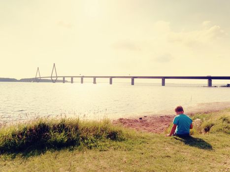 Boy is playing game on offshore, view to the  big traffic bridge over sea . The two road bridge with high rope towers connect the islands.