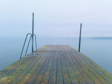 Abandoned wooden wharf mole in sea within sunrise. Gentle blue pink color of sky blurry waves on water level.