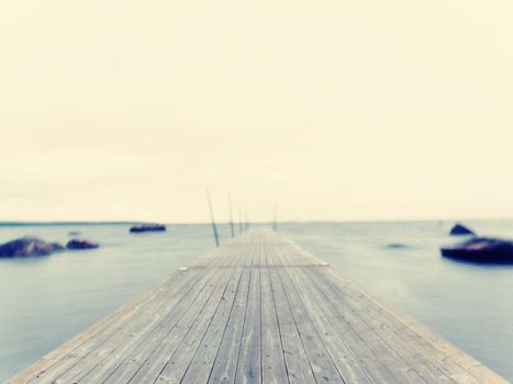 Empty wooden mole in water of blue lake.  Old fishing wharf for hired boats and swimmers. Waves smooth by long exposure, cloudy sky.