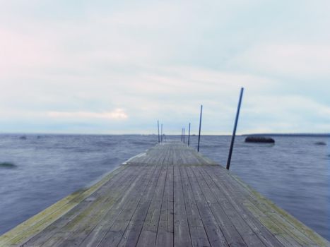 Empty wooden mole in water of blue lake.  Old fishing wharf for hired boats and swimmers. Waves smooth by long exposure, cloudy sky.