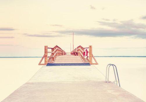 Long wooden sea bridge on coast during morning. Cold weather with first sun rays at horizon, smooth water. New built  pier in summer holiday resort. Empty mole.