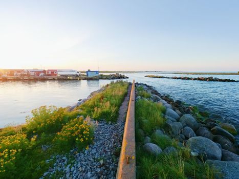 Small fishing port with boats anchored and  moored on  sea bay in Sweden. Built stony dam, wooden pier, red and white houses.