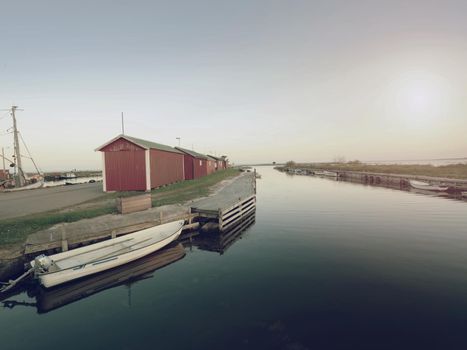 Small fishing port with boats anchored and  moored on  sea bay in Sweden. Built stony dam, wooden pier, red and white houses.