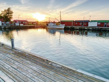 Small fishing port with boats anchored and  moored on  sea bay in Sweden. Built stony dam, wooden pier, red and white houses.