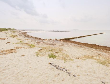 Wooden breakwaters on a shore of the Baltic Sea with a sun hidden in low clouds. Smooth water level after storm.