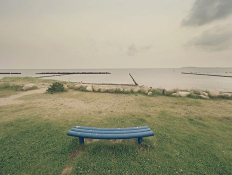 Stony beach and blue bench. Bench by the sea in the cloudy sunrise