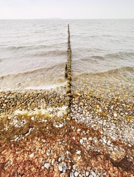 Wooden breakwater in wavy Baltic Sea. Evening at smooth wavy sea. Pink horizon with low clouds