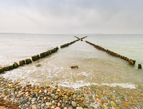 Wooden breakwaters on a shore of the Baltic Sea with a sun hidden in low clouds. Smooth water level after storm.