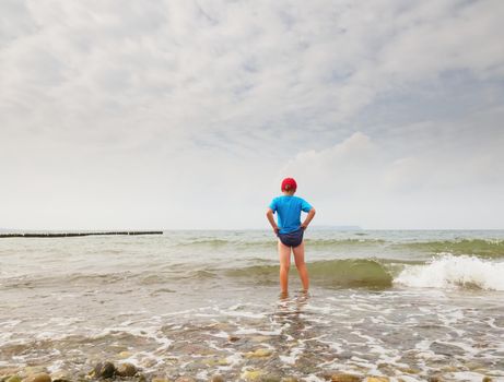 Children on the beach go into the ocean. Kid play in the waves of foamy sea.