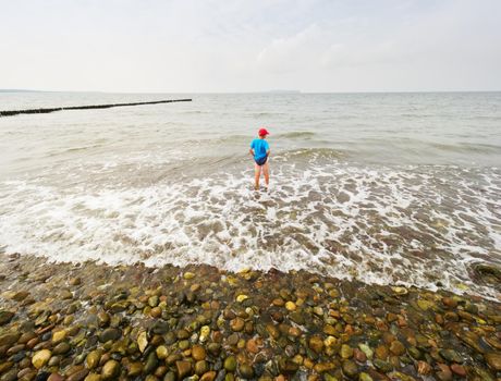 Children on the beach go into the ocean. Kid play in the waves of foamy sea.