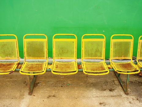 Vintage steel seats on outdoor stadium players bench chairs with worn paint below green wall