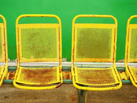 Old yellow rusty metal seats on outdoor stadium. Players bench chairs with poor paint 