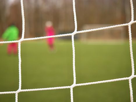 Football player stands against goal with net and stadium. Football gate net. Soccer gate net.  In blurry background stand people.