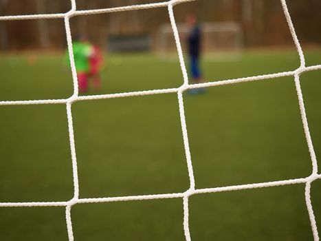 Football player stands against goal with net and stadium. Football gate net. Soccer gate net.  In blurry background stand people.