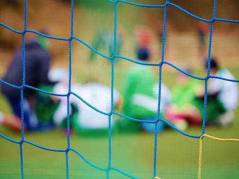 Footballists and stadium arena soccer field defocused. Vew through soccer gate net. 
