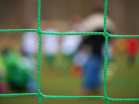Football player stands against goal with net and stadium. Football gate net. Soccer gate net.  In blurry background stand people.
