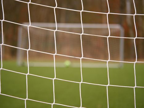 Football player stands against goal with net and stadium. Football gate net. Soccer gate net.  In blurry background stand people.