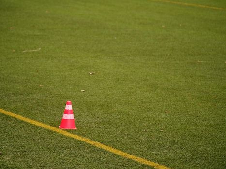Bright red plastic cone on painted white line of soccer field. Football green playground with  rubber cone