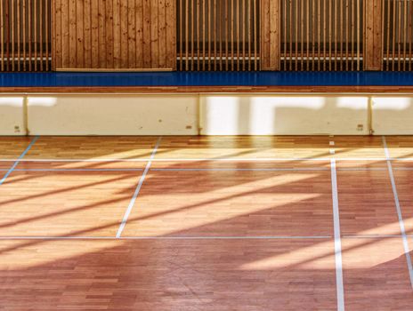 Schooll gym hall with water heating system hidden over wooden bars cover.  Basketball court. Lines of playfield in hall.