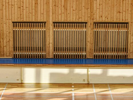 Schooll gym hall with water heating system hidden over wooden bars cover.  Basketball court. Lines of playfield in hall.