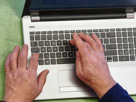 Working on laptop close up of hands of old man. Closeup hand of business man using laptop at office. Close up view of man hands business working on laptop 