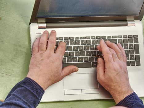 Working on laptop close up of hands of old man. Closeup hand of business man using laptop at office. Close up view of man hands business working on laptop 