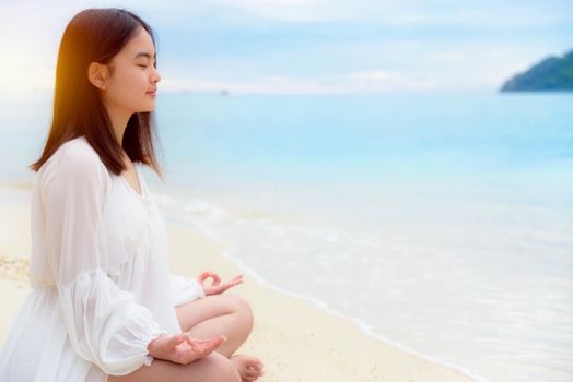 Beautiful asian young woman practice yoga on the beach near the sea under sunlight at sunrise, Relaxation for health in the midst of nature with happiness and peace, blank for the background