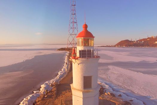 Aerial view of the pink sunset over the Amur Bay on the background of a white lighthouse.
