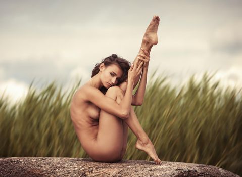 Beautiful young nude woman on blurred nature background. High-contrast image with intentional color shift