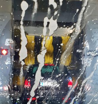 A car is washing in a car wash, a view through the wet windshield. The brushes washing a car in a car wash.